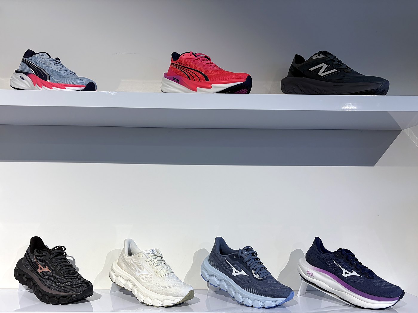 Dames hardloopschoenen van Puma, New Balance en Mizuno aan de wand bij Sport-Inn Bussum